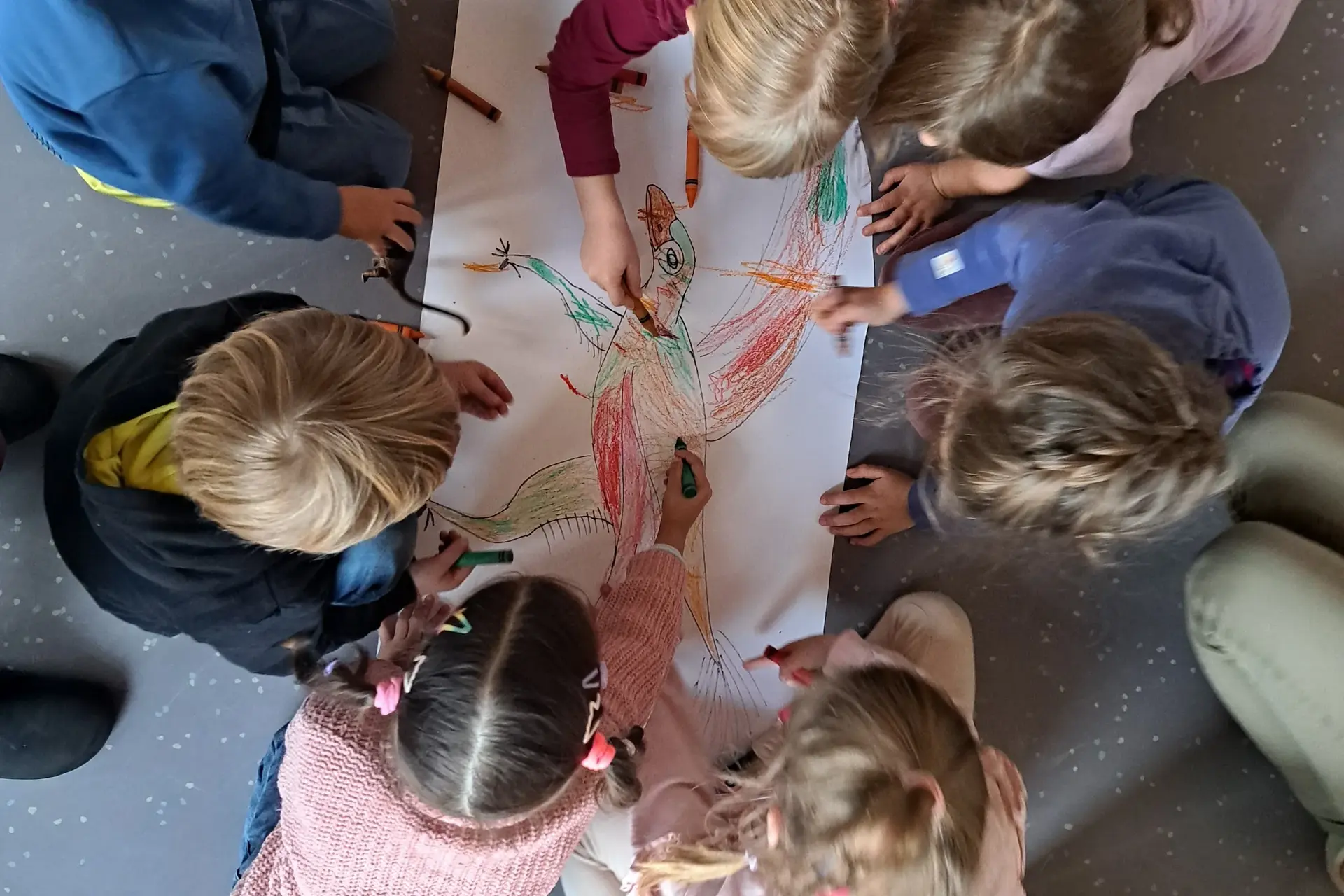 Kinder sitzen im Kreis auf dem Boden und malen gemeinsam ein buntes Tier
